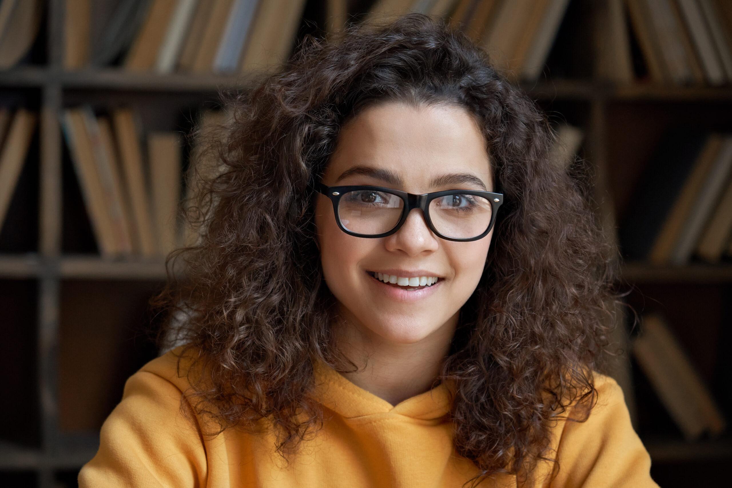 Young girl with glasses and long curly hair smiling in a library 