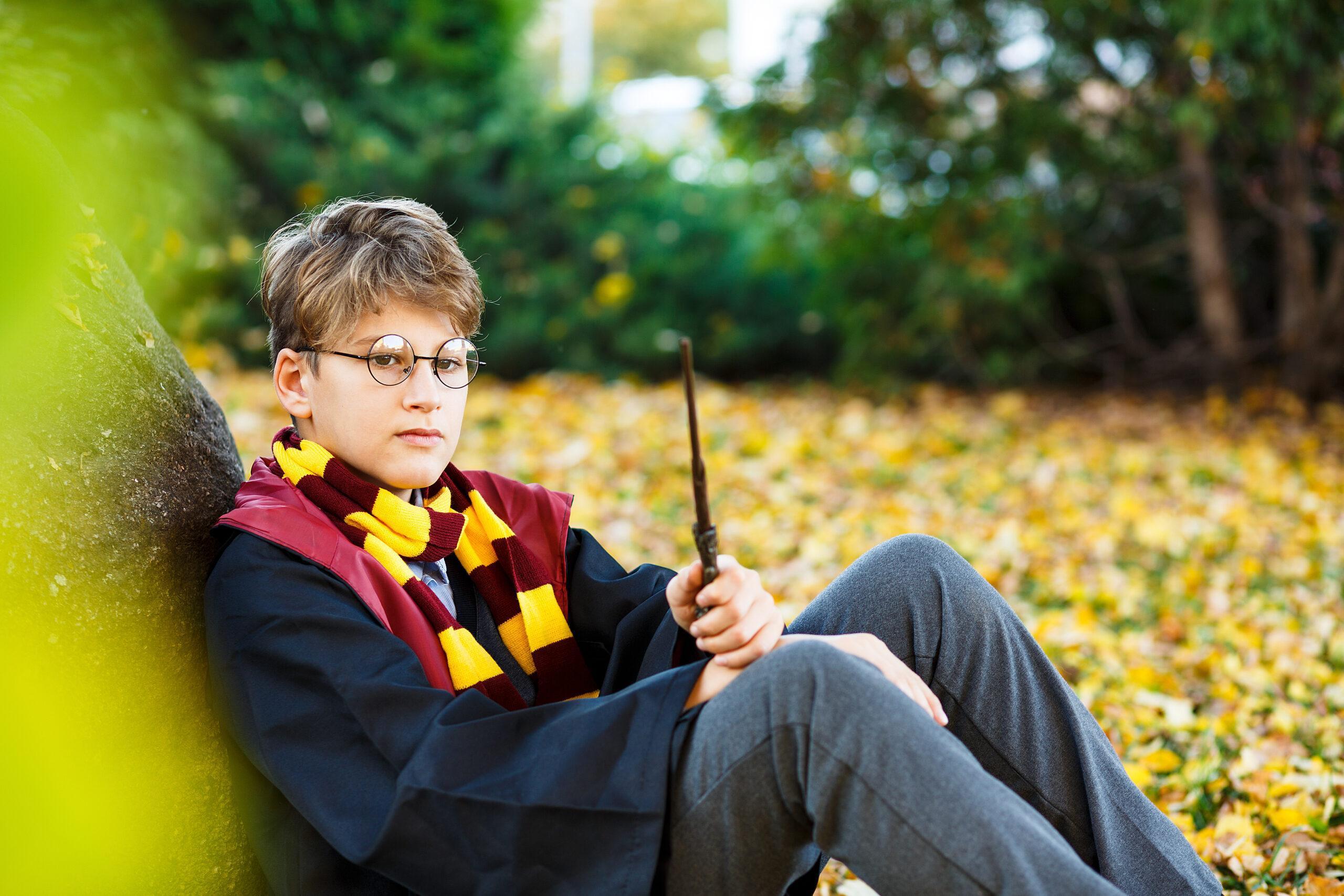 A Harry Potter fan sitting by a tree holding a wand 