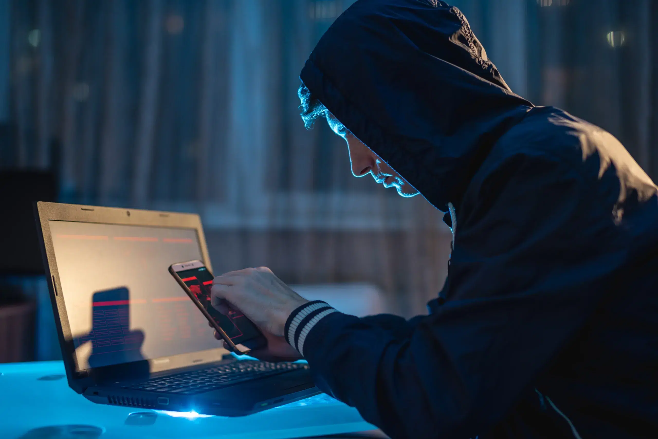 Male hacker in the hood holding the phone in his hands trying to steal access databases with passwords. Cybersecurity