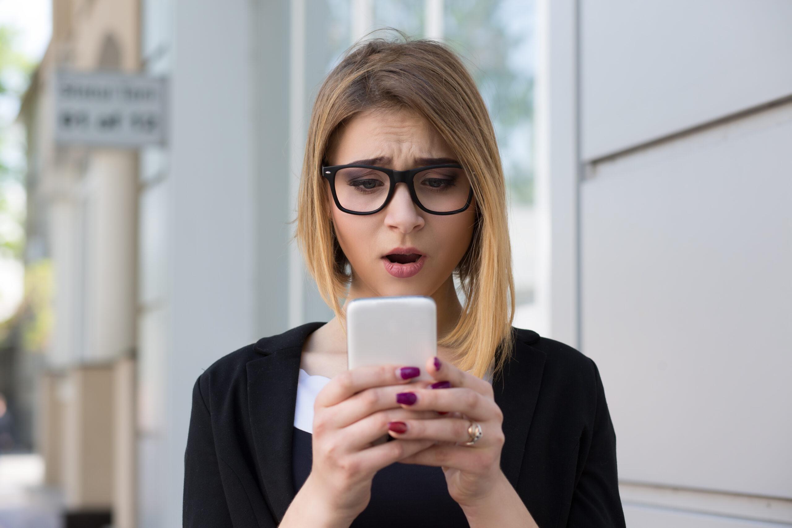 Anxious young girl looking at phone seeing bad news