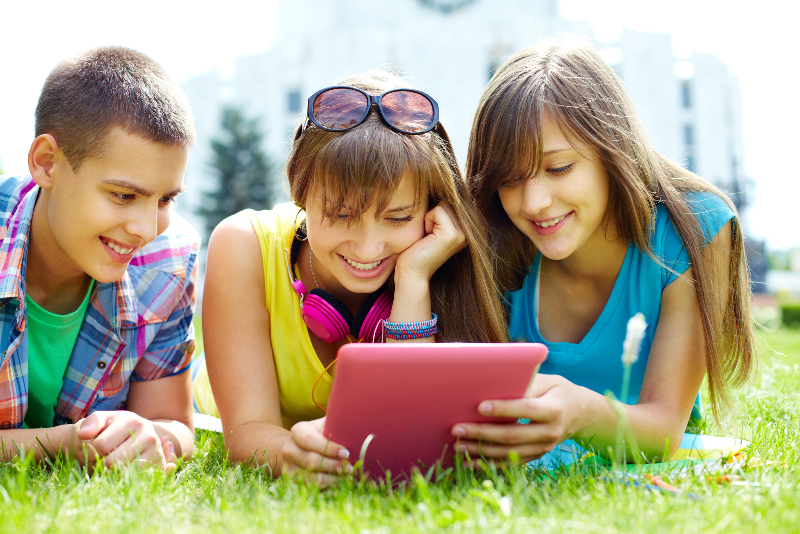 young kids having fun sitting on the grass watching a video together on a digital tablet