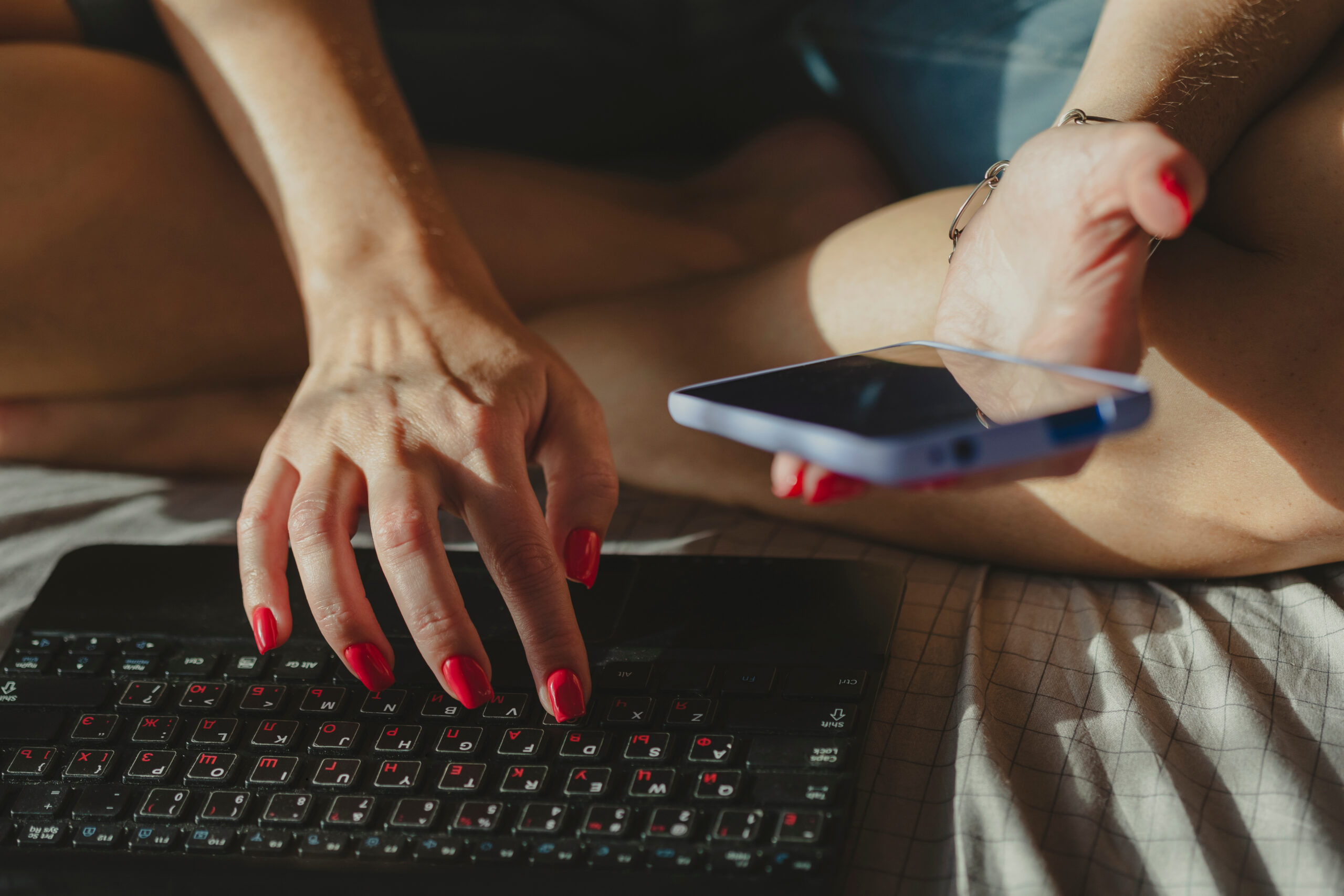 Young woman typing on laptop and using cell phone