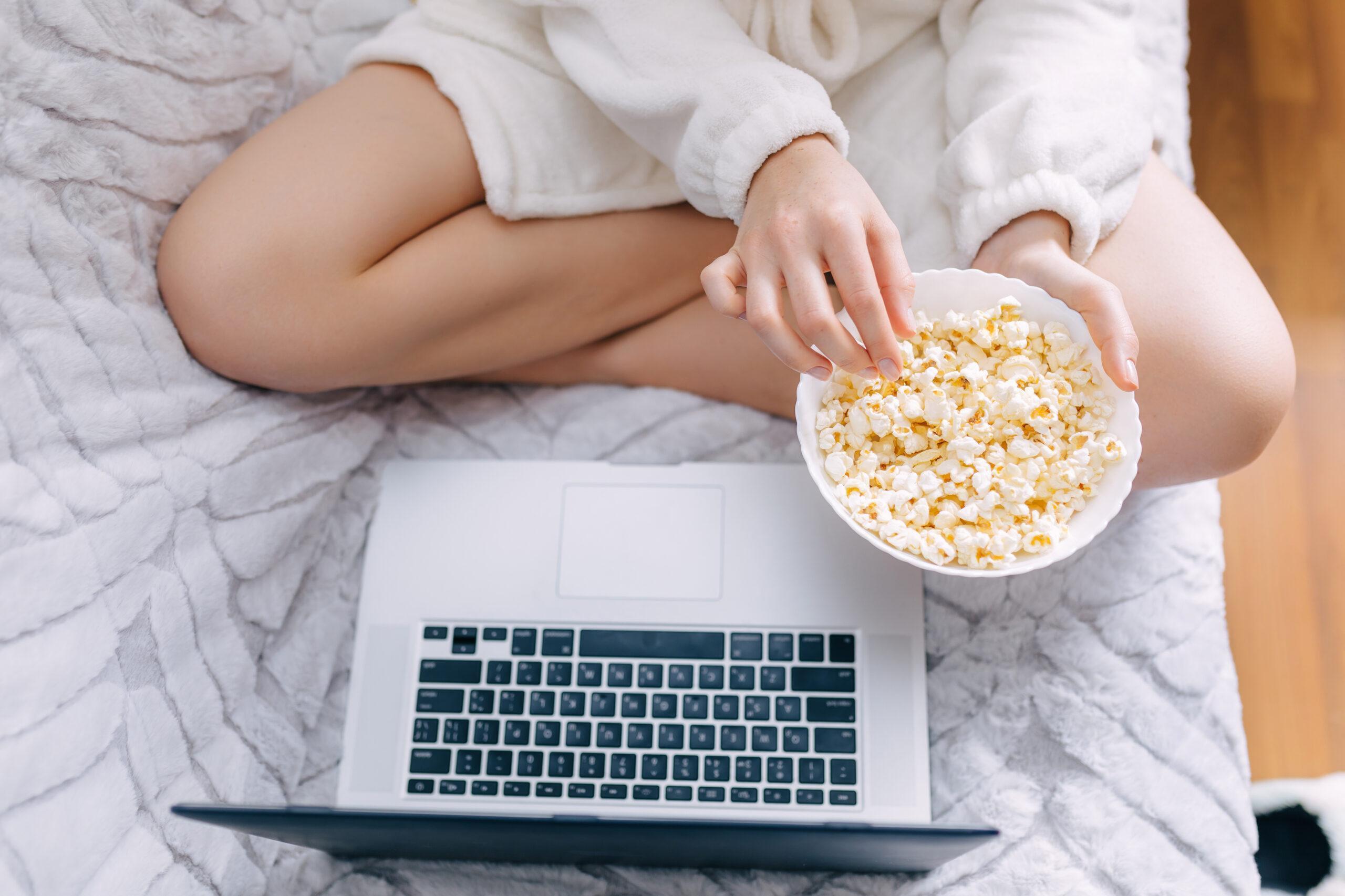 Woman eating popcorn while watching on her laptop