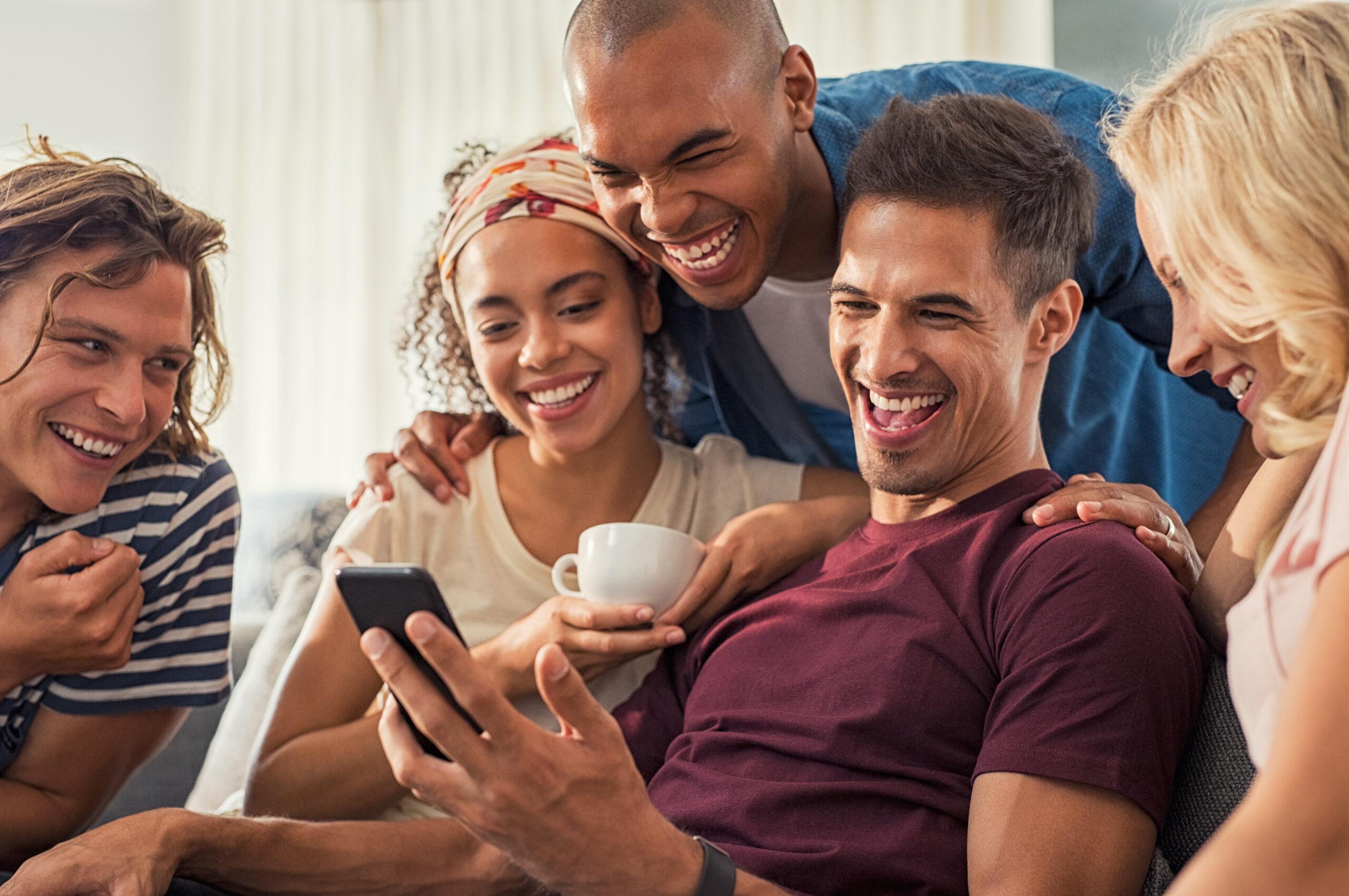 Happy friends laughing together at a meme they see on one guy's cellphone