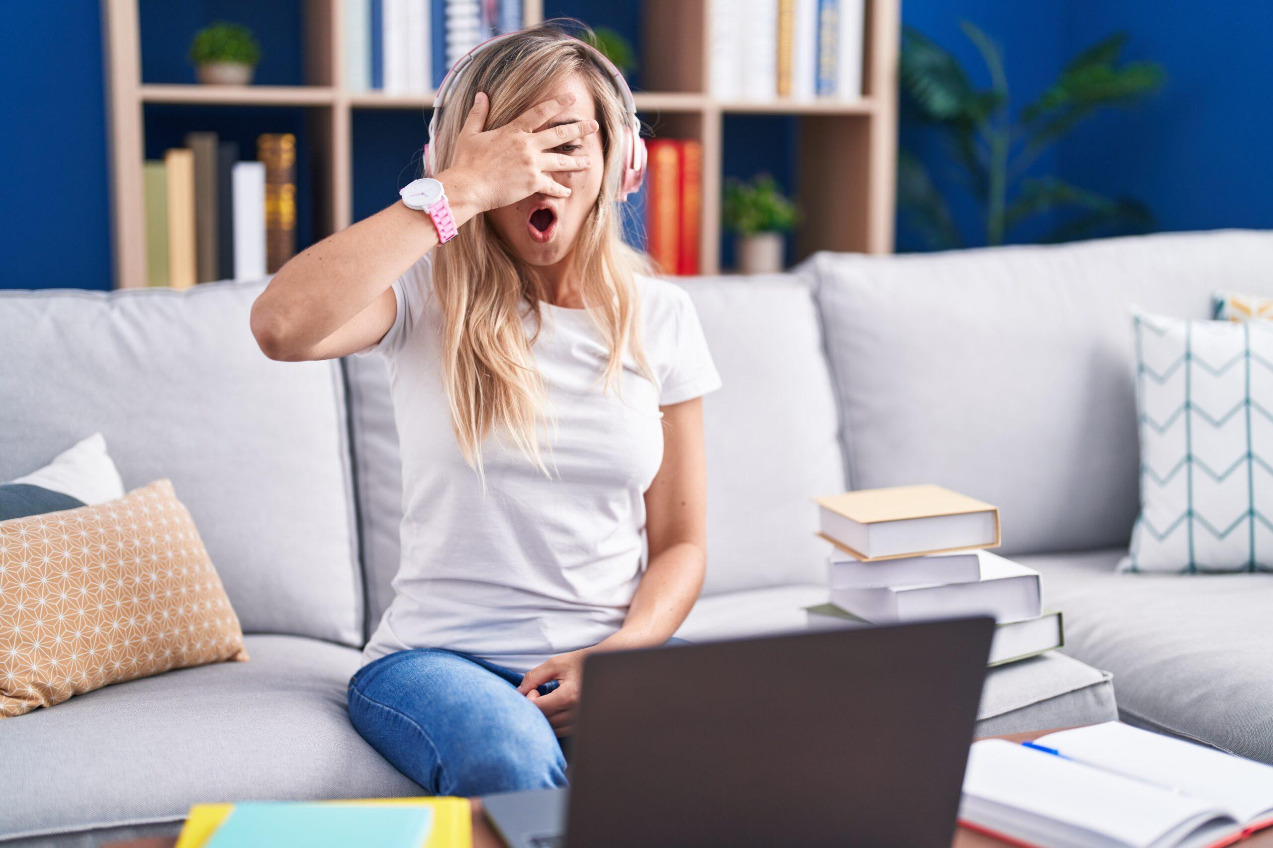 Blonde woman with headphones covering her eyes while watching  a show on her laptop