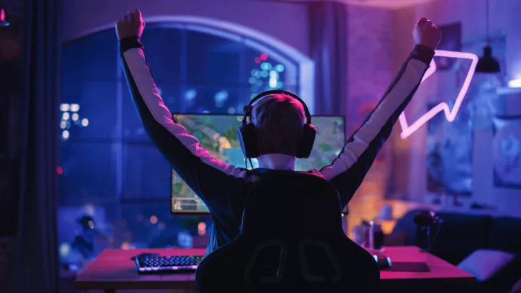 Successful young female gamer wearing headphones and raising her hands in victory 