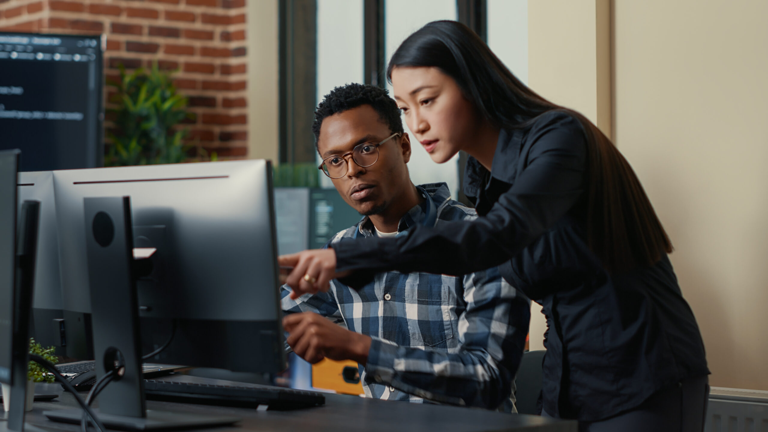 Two software developers coming at desk and sitting down holding laptop with coding interface