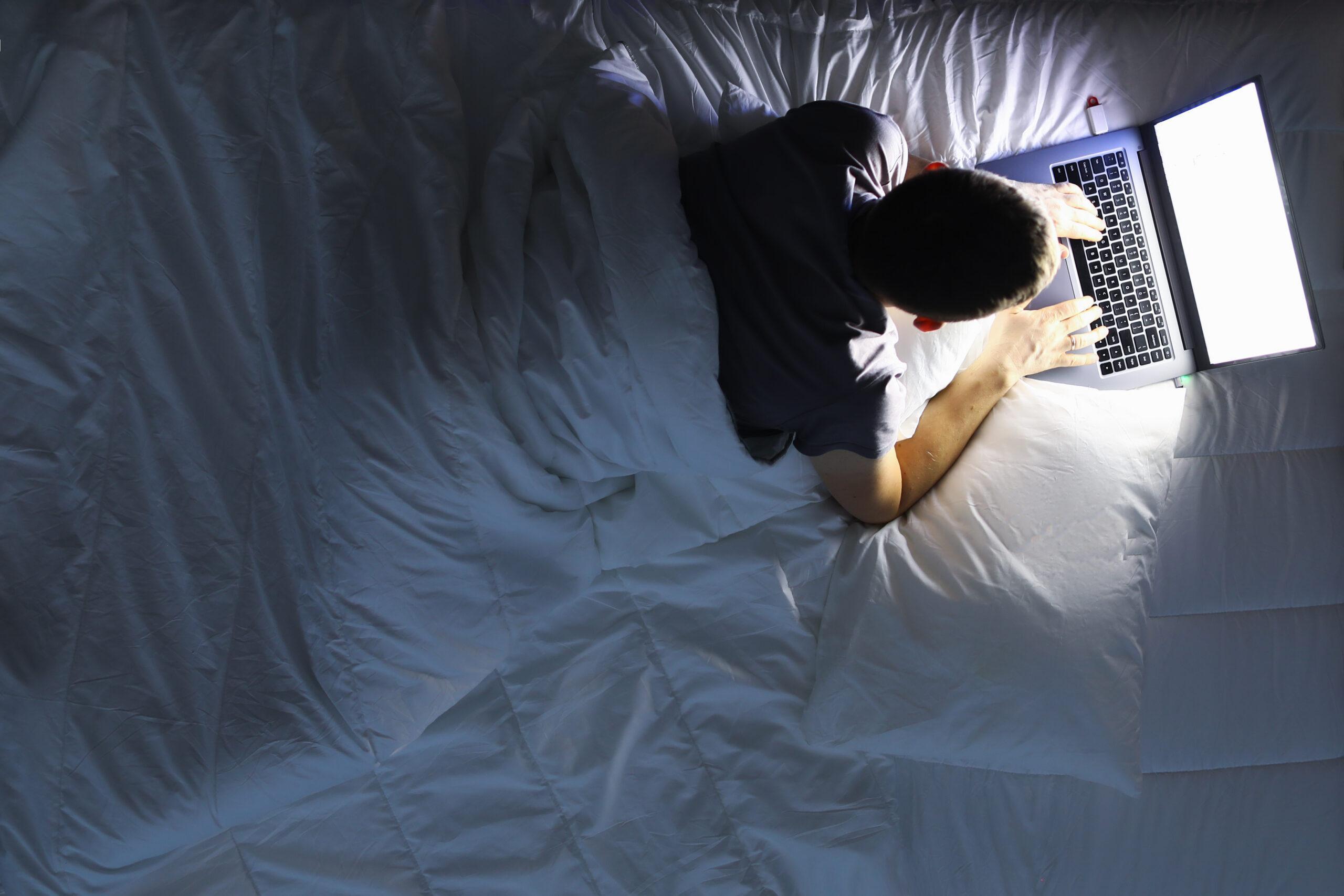 Man in bed with laptop using internet in online service love chat 