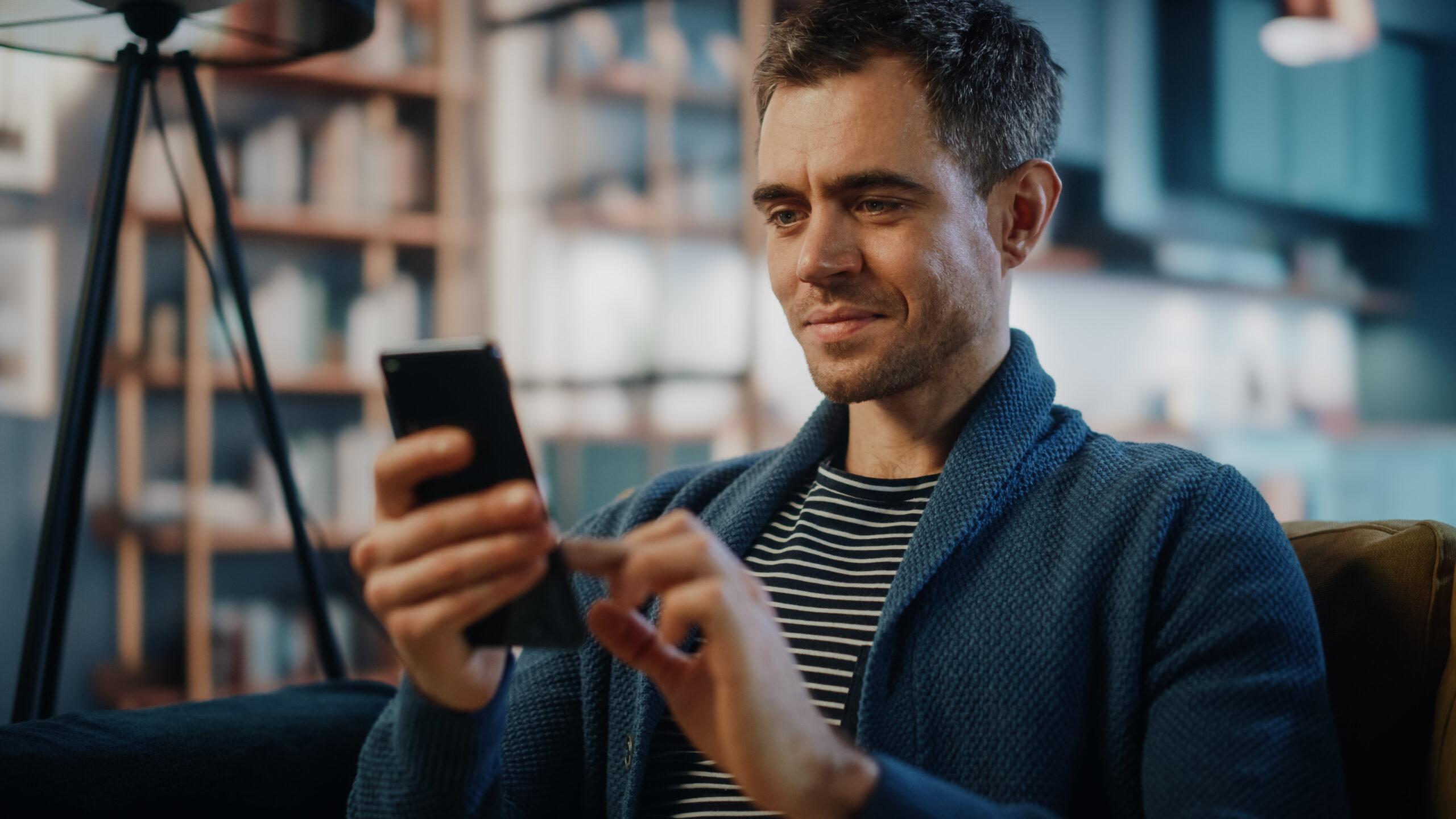 Excited man using smartphone while resting on a sofa in stylish living room