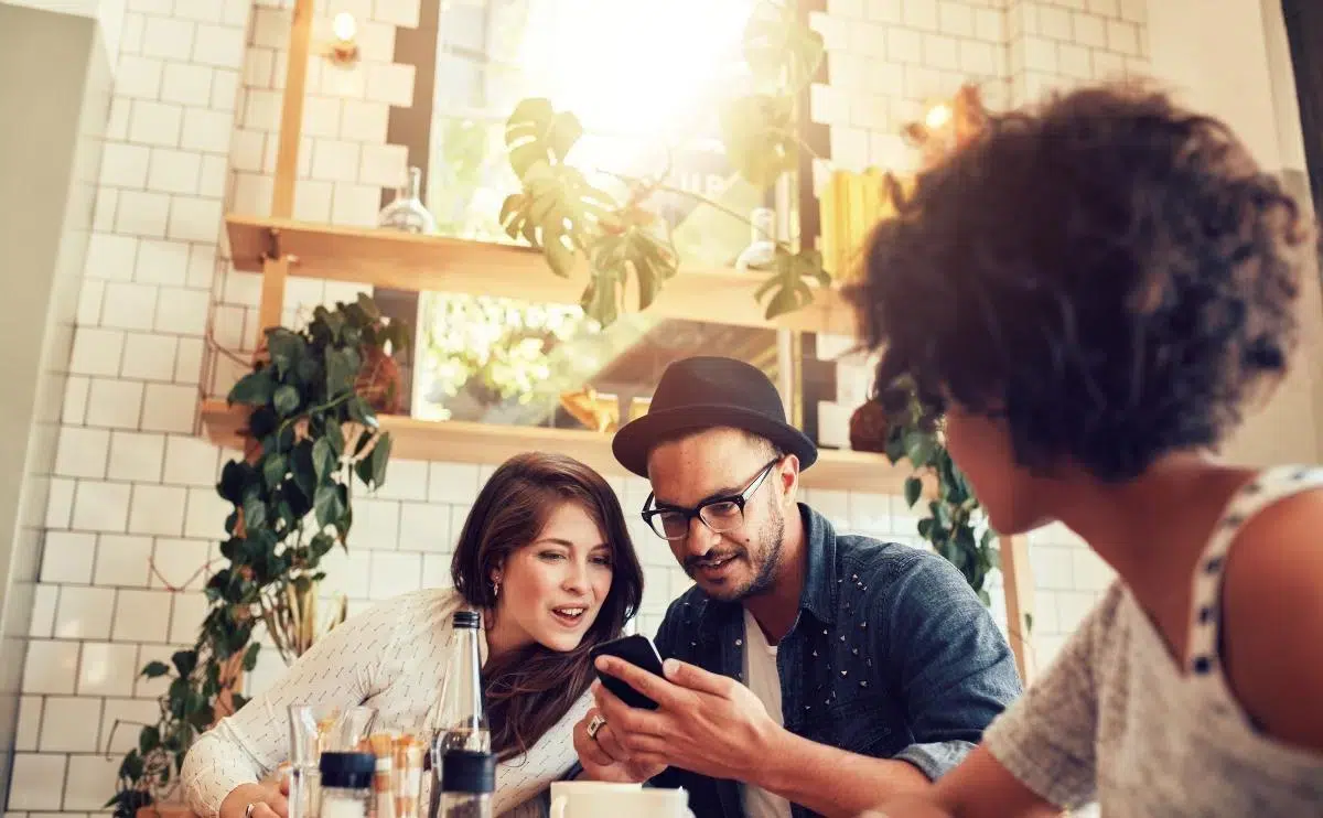 Young couple looking at smart phone while sitting in cafe with friends