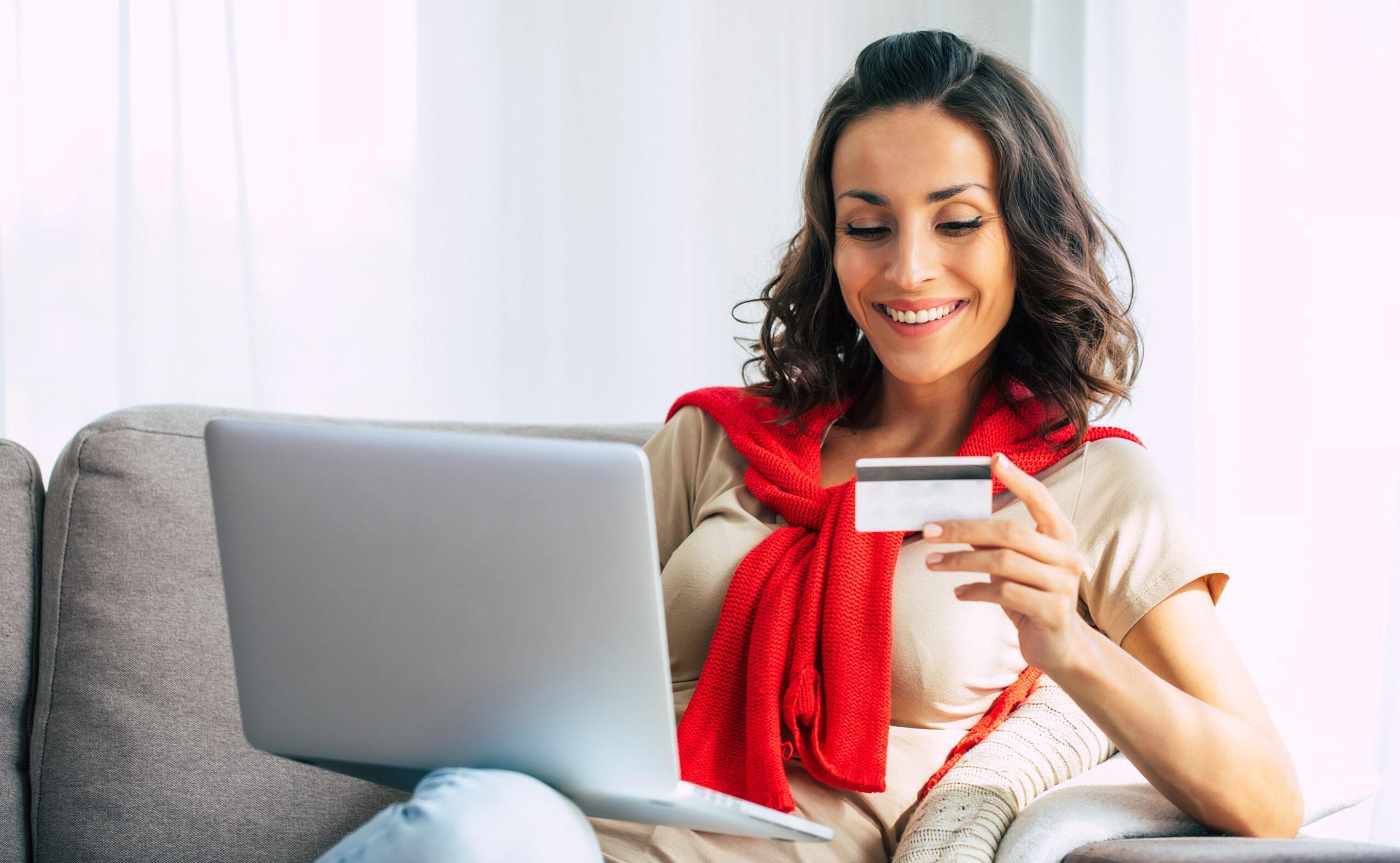 Beautiful happy young woman in casual clothes is sitting on the couch and checking credit card info she typed on laptop is accurate