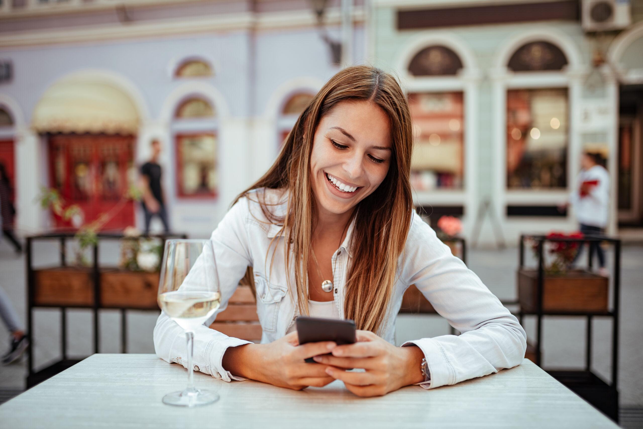 Young woman laughing while using phone at outdoor restaurant