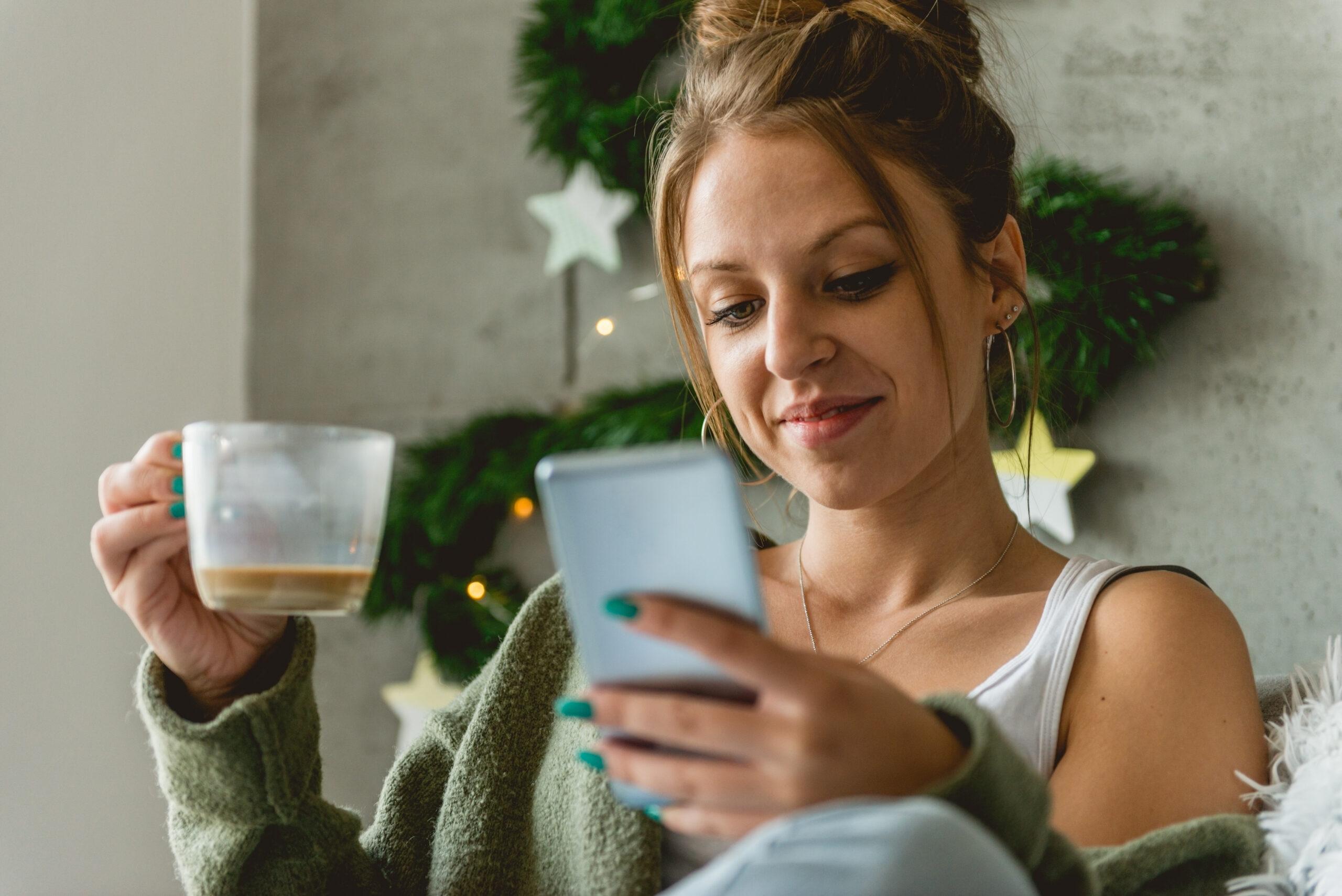 Woman checking her smartphone while drinking coffee early in the morning
