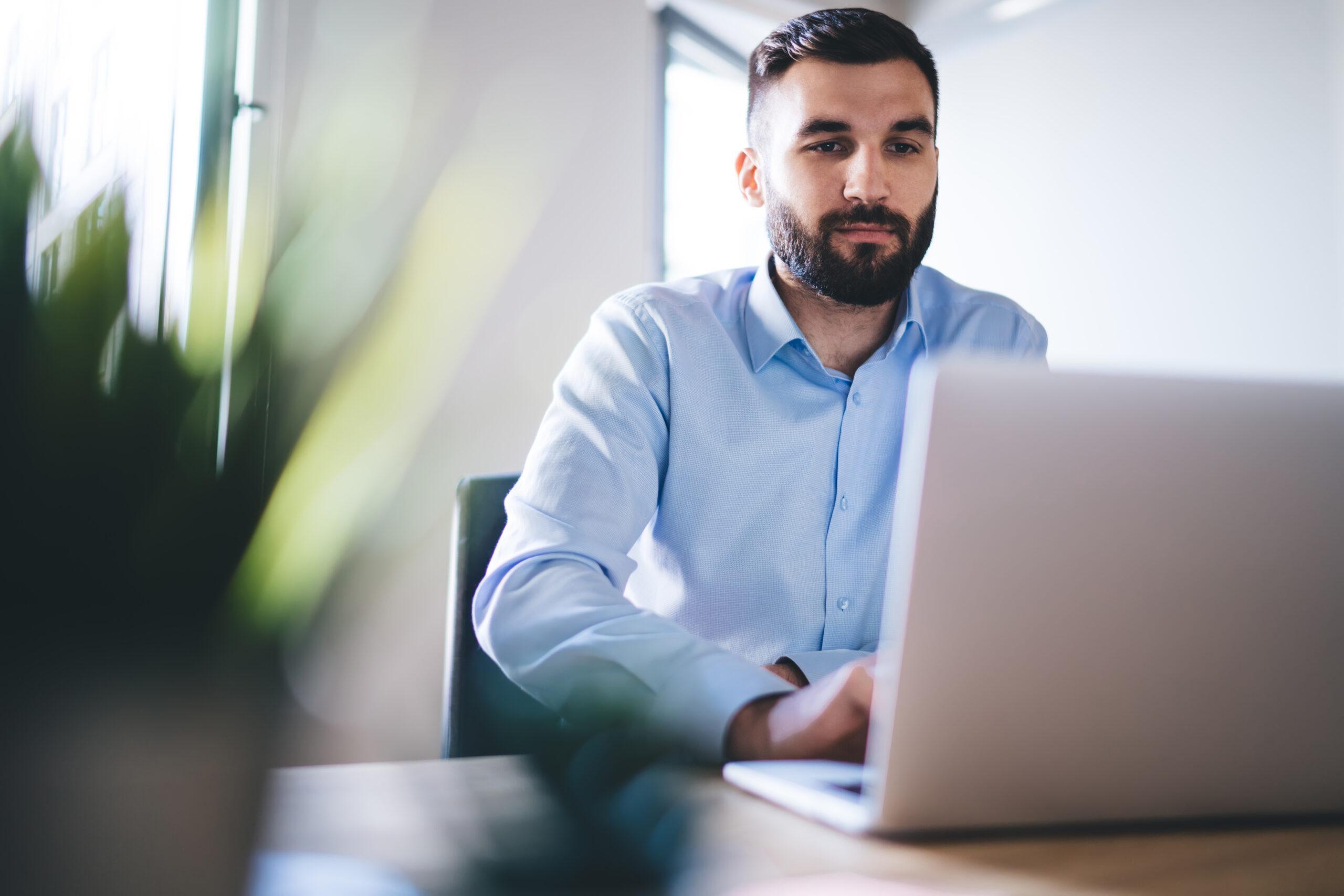 Confident bearded millennial typing on laptop 