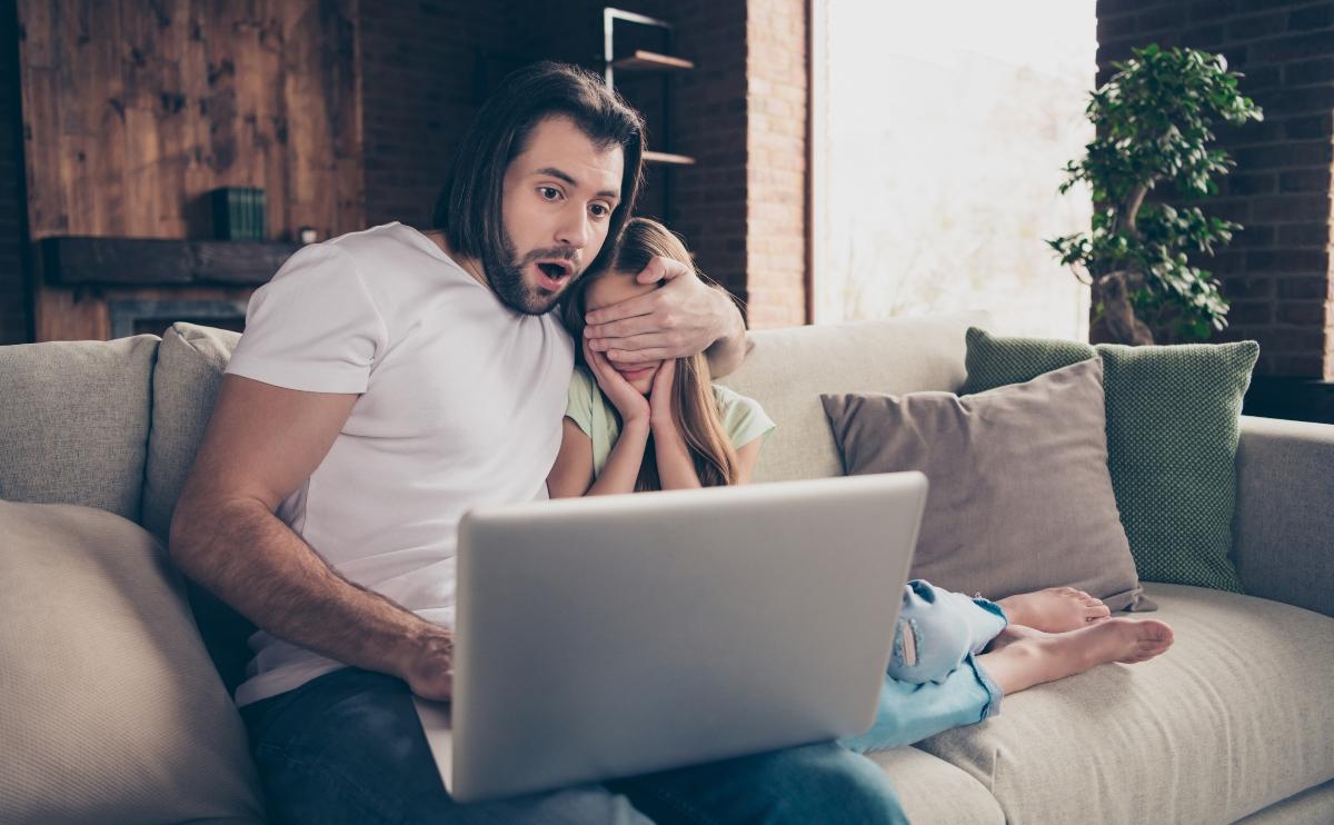 Father covering her daughter's eyes as an inappropriate scene plays on the laptop 
