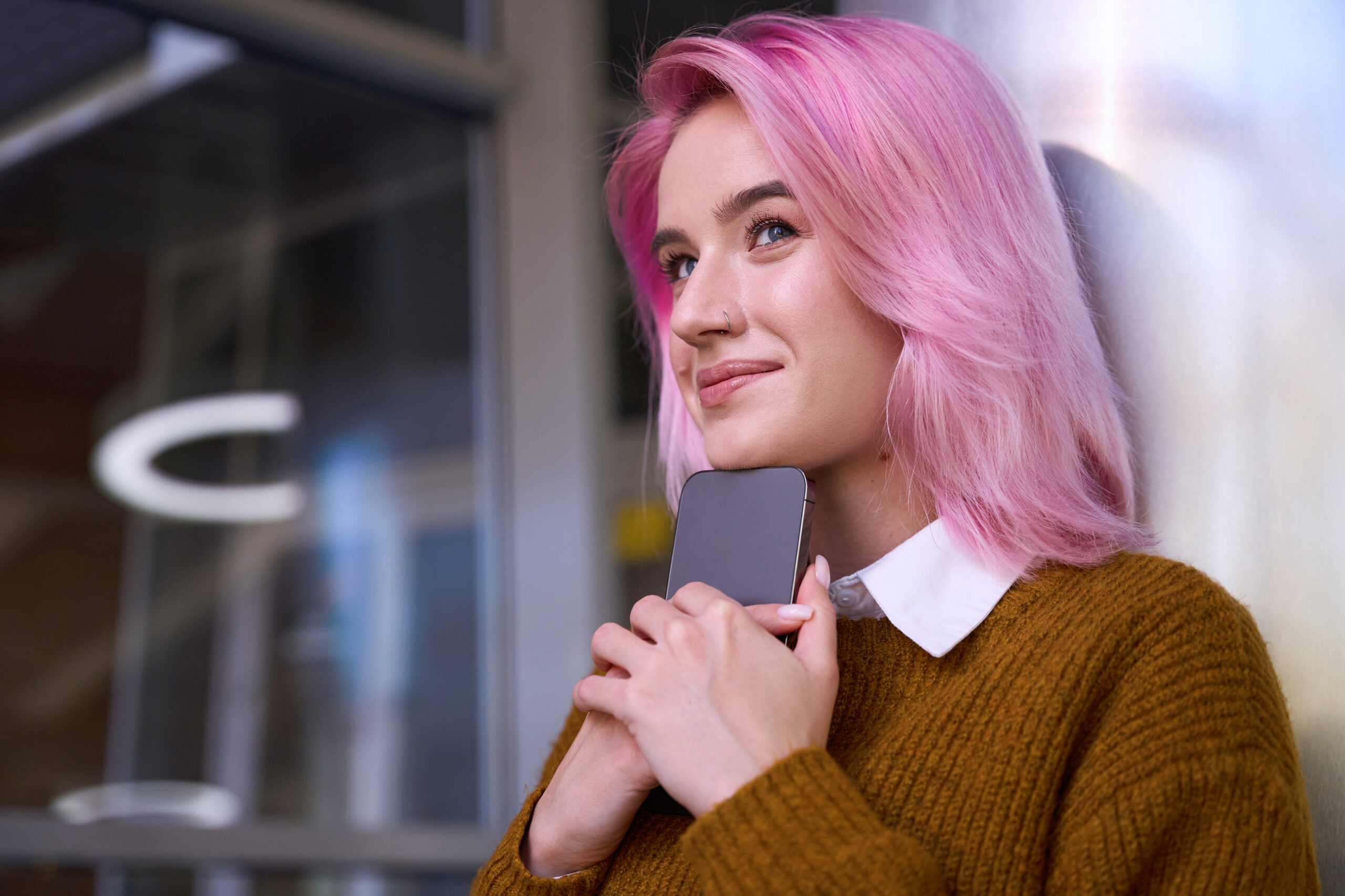 Smiling young lady with pink hair holding her smart phone close to her