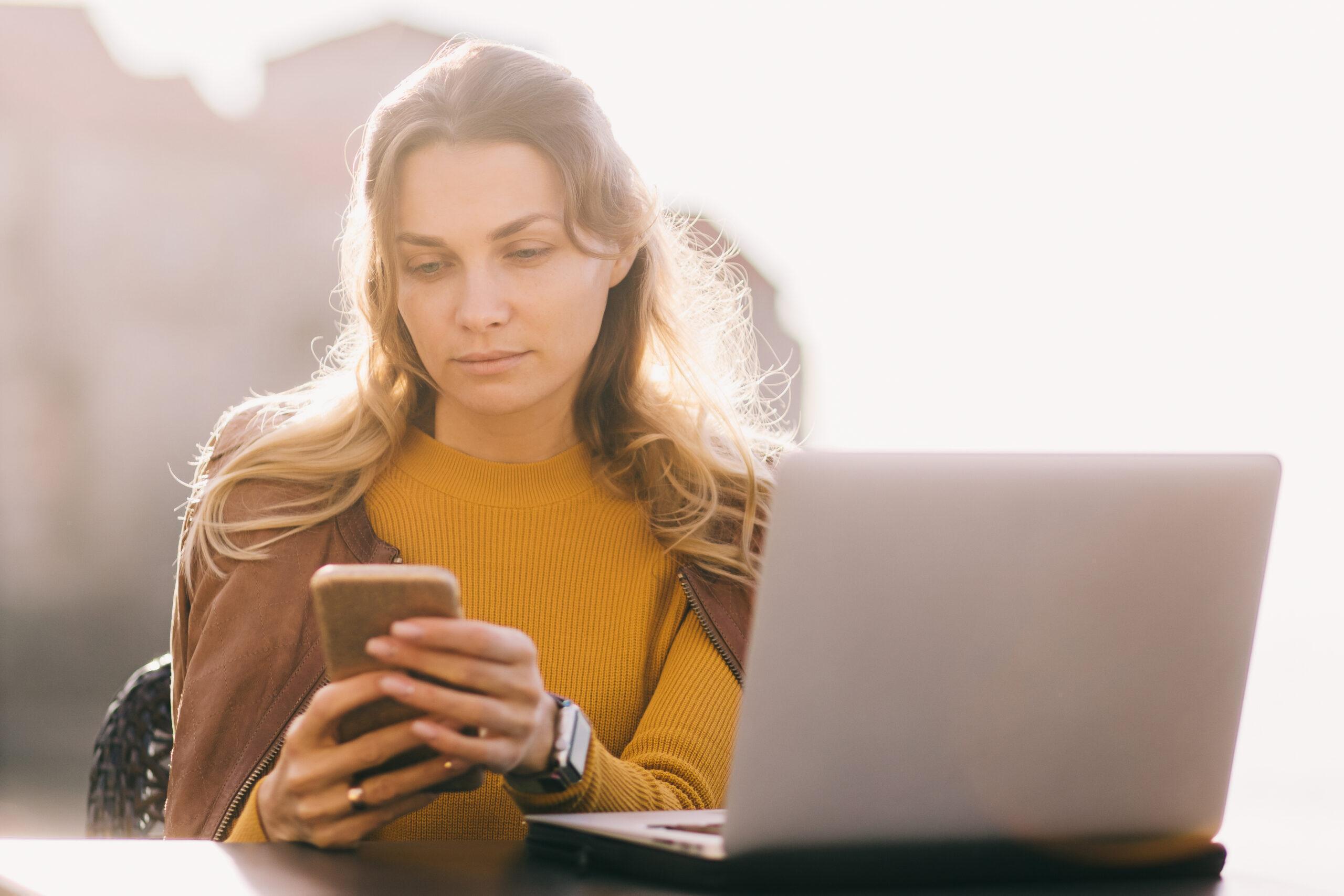 Serious young business woman work on laptop and smartphone outdoors. Female entrepreneur solving problem chatting on phone