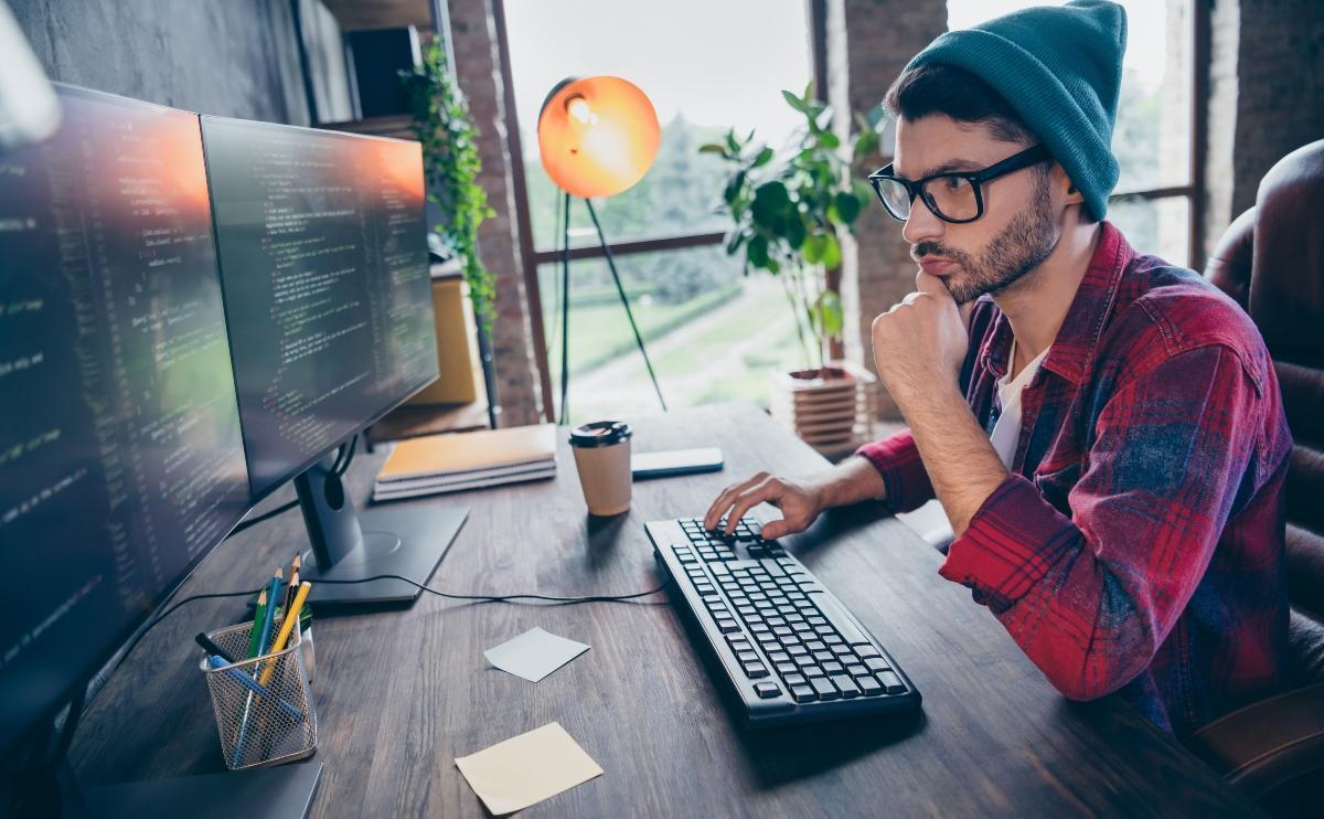 Photo of smart intelligent coder dressed hat glasses writing application software modern gadget indoors workplace workstation loft