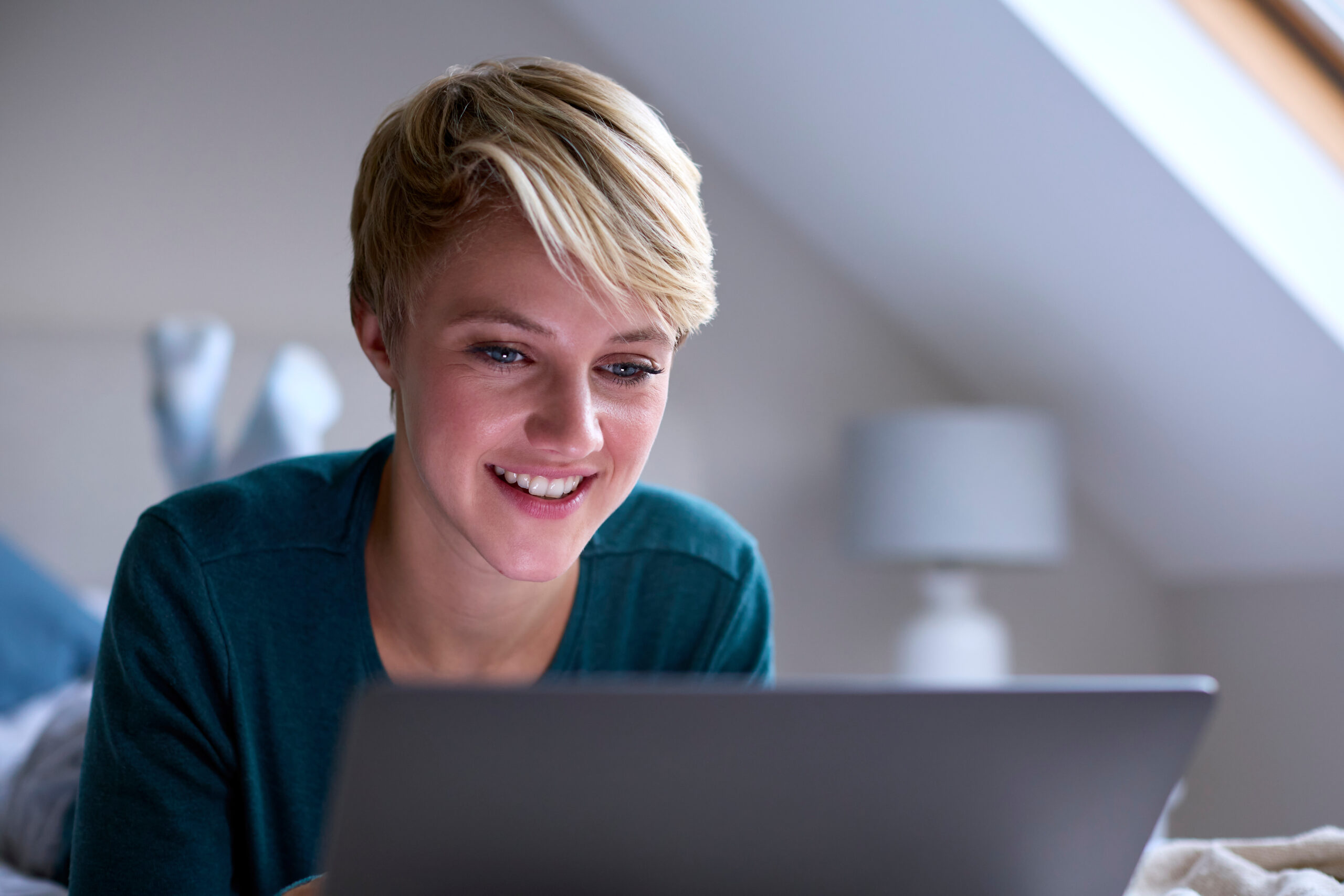 Young blonde lady smiling while using her laptop at home