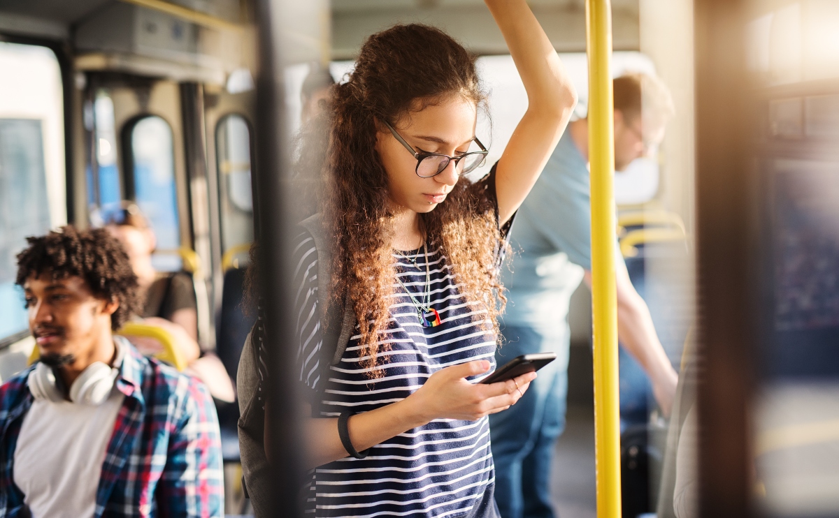 Young girl with glasses standing in a bus while checking her phone