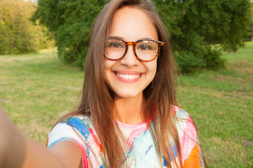 Young woman with glasses taking a selfie outdoor.