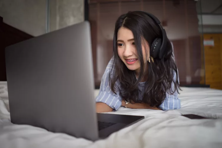 Girl with headphones watching movie with laptop on the bed