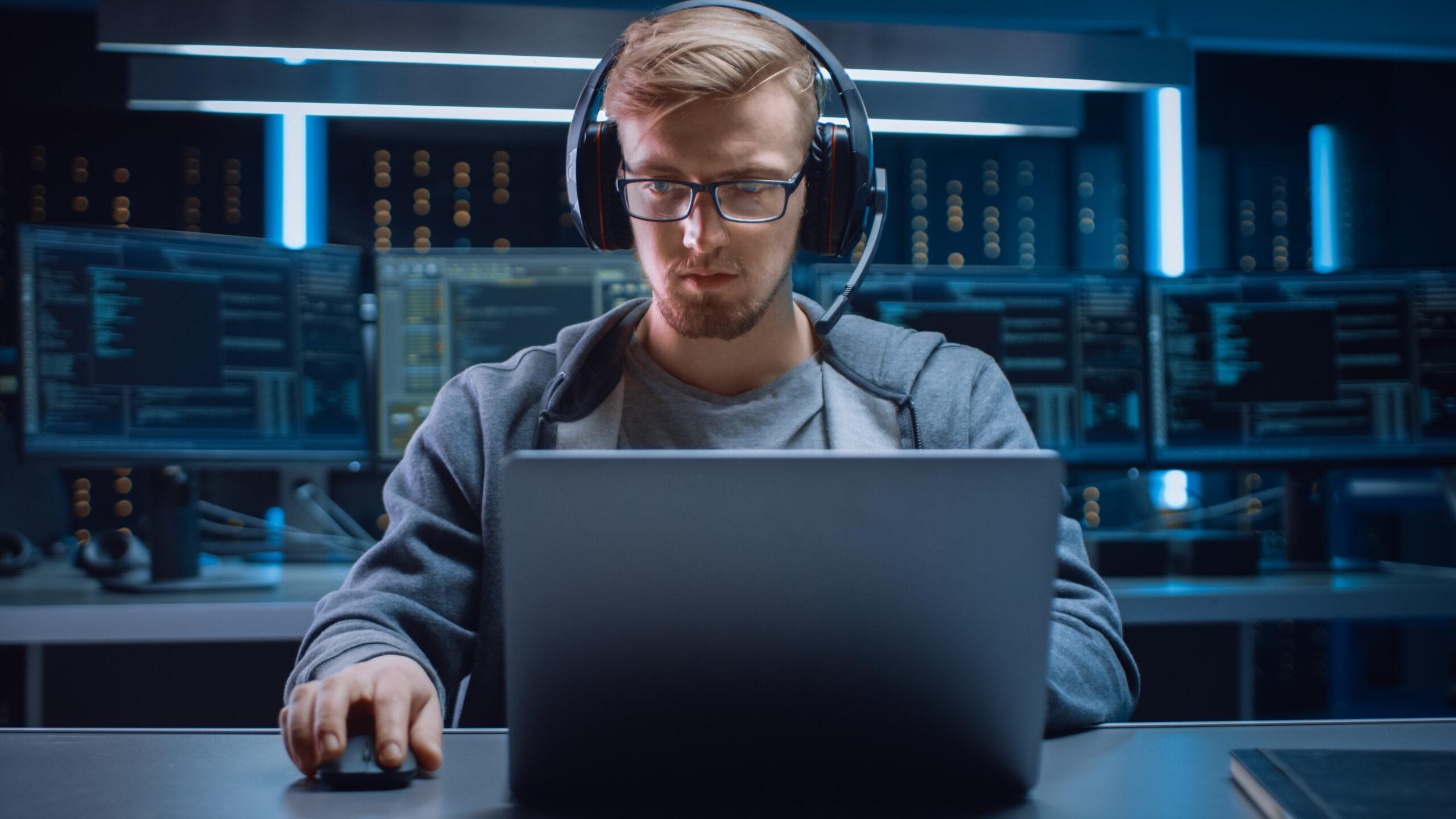 With servers behind him, programmer with glasses working on his computer 