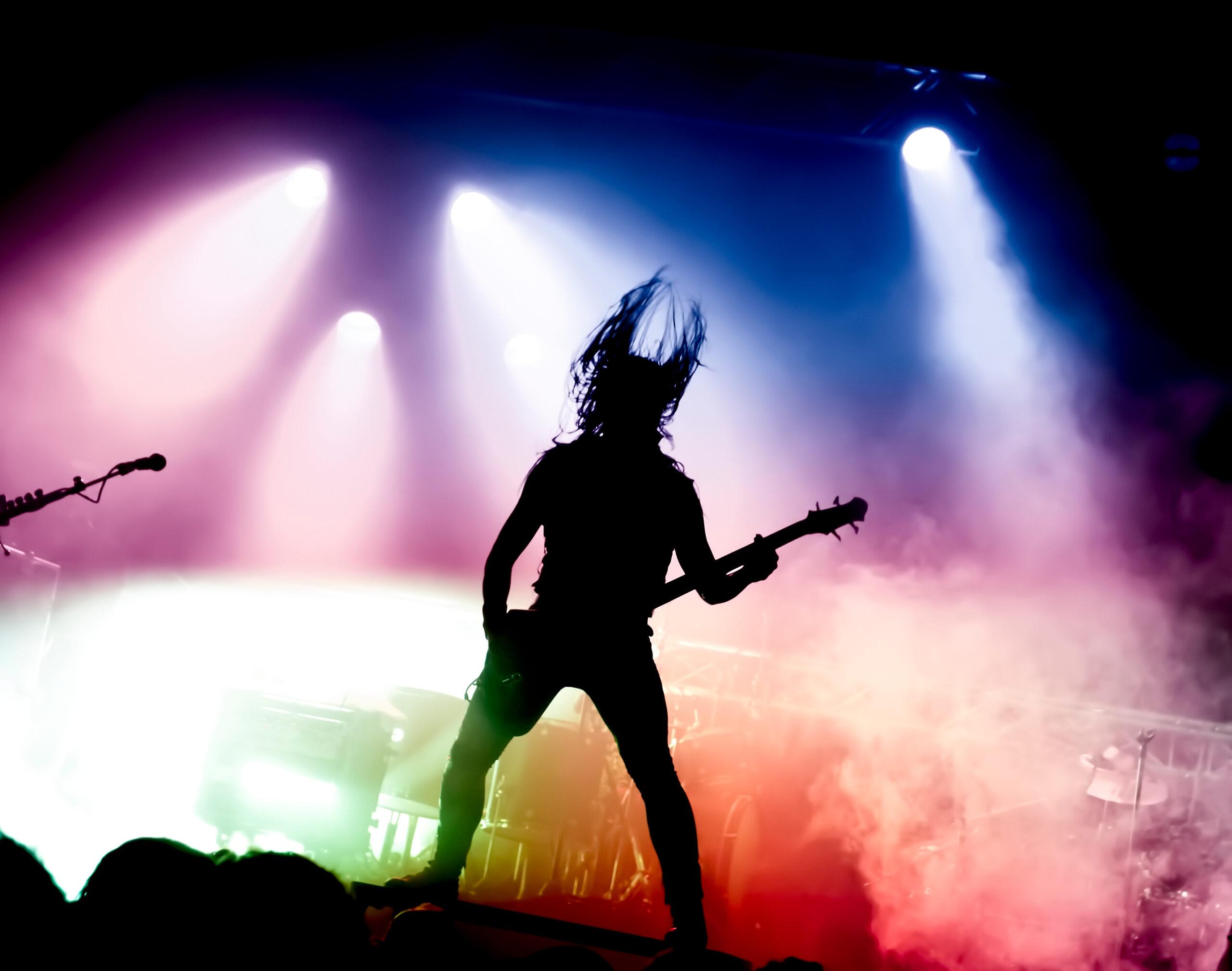 silhouette of guitar player in action on stage in front of conce