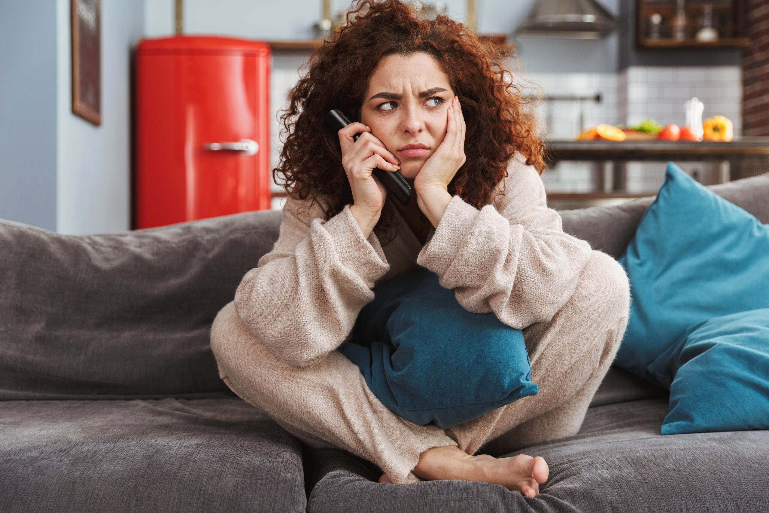 Frustrated young woman with remote sitting on sofa in apartment 