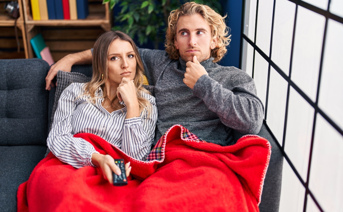 Young couple sitting on the sofa at home, hands on chin, both thinking about confusing idea