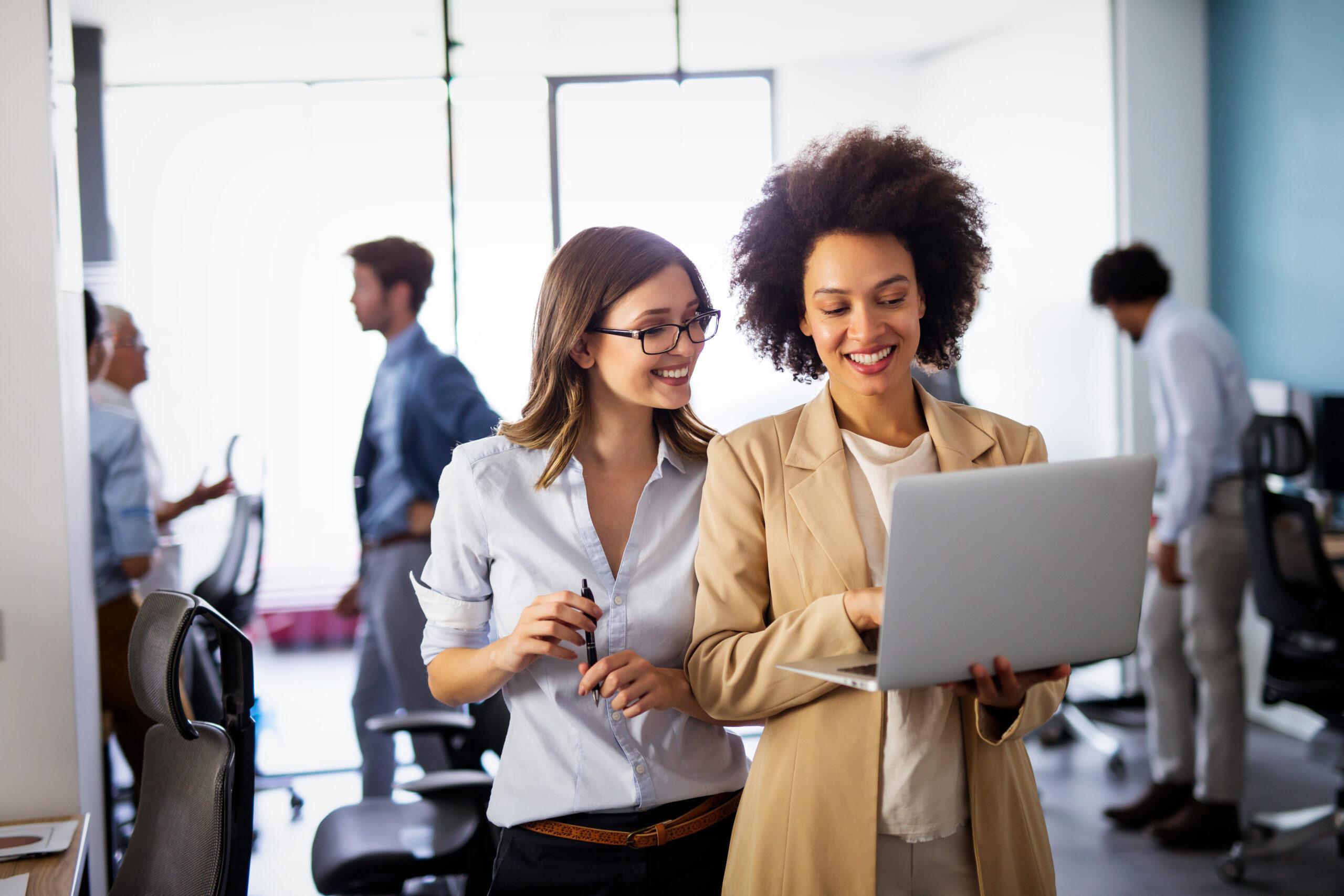 Happy multiethnic business women working together online on a laptop in corporate office.