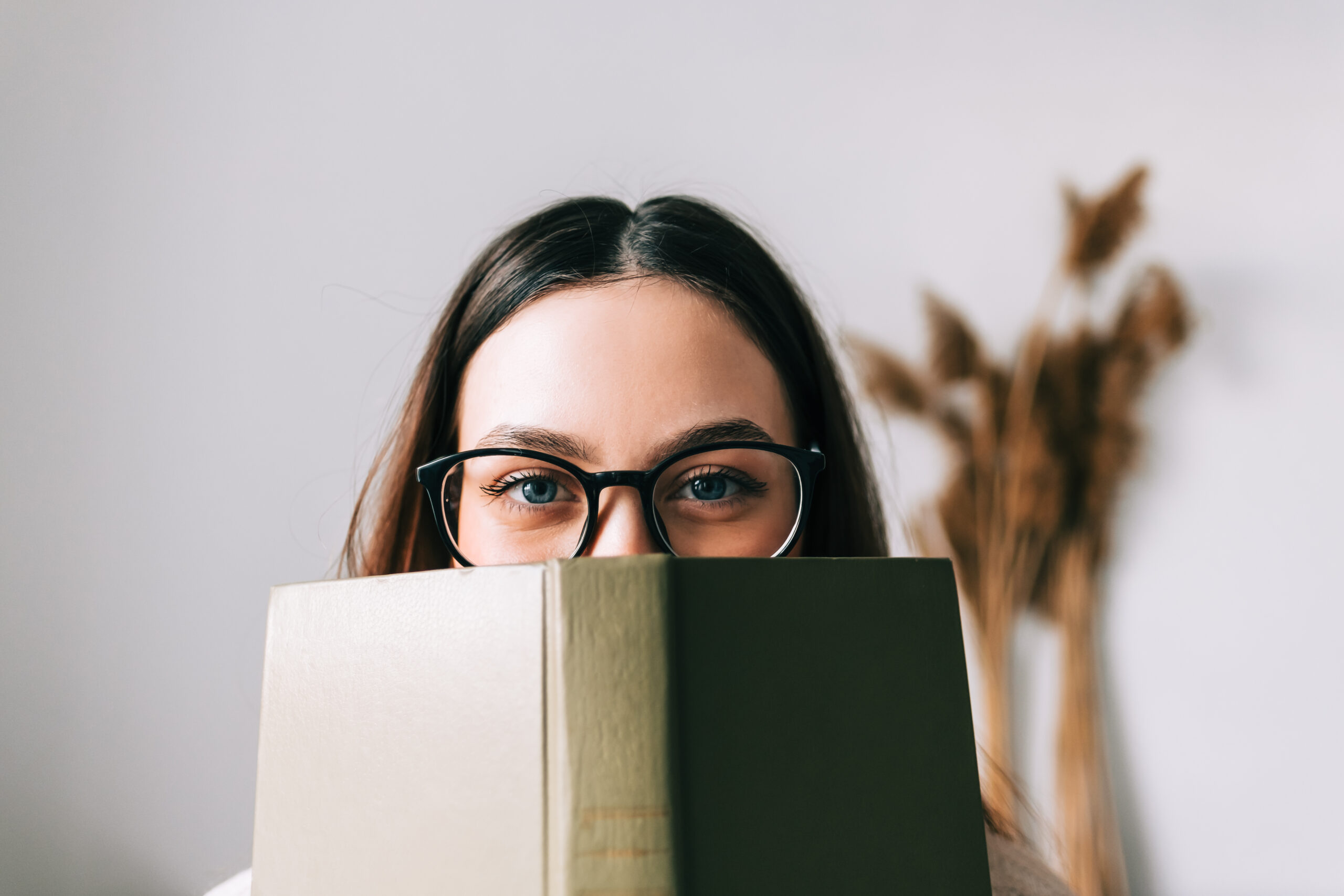 Woman with glasses hiding behind a book