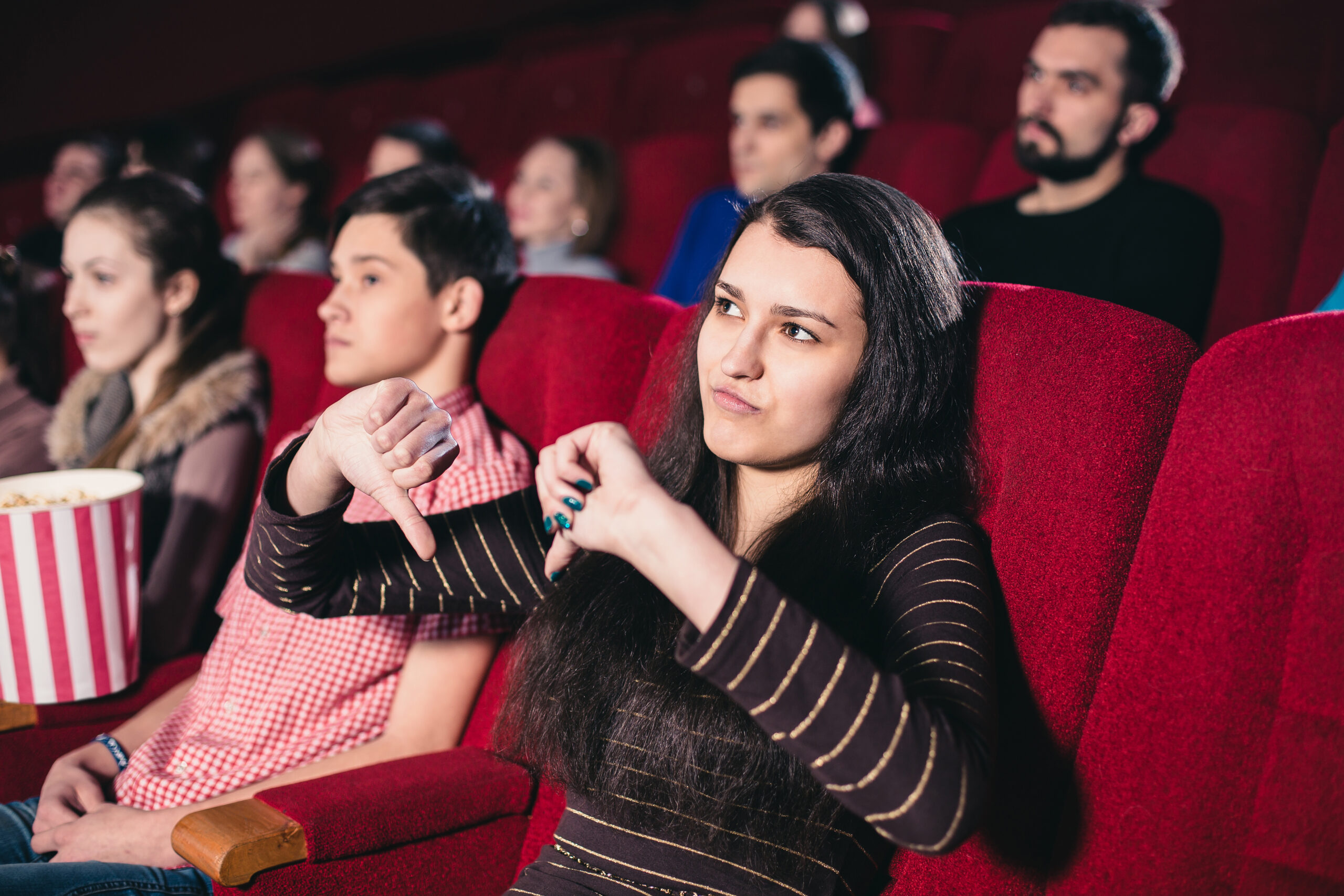 Girl in a movie theater giving a thumbs down sign to a movie she doesn't like