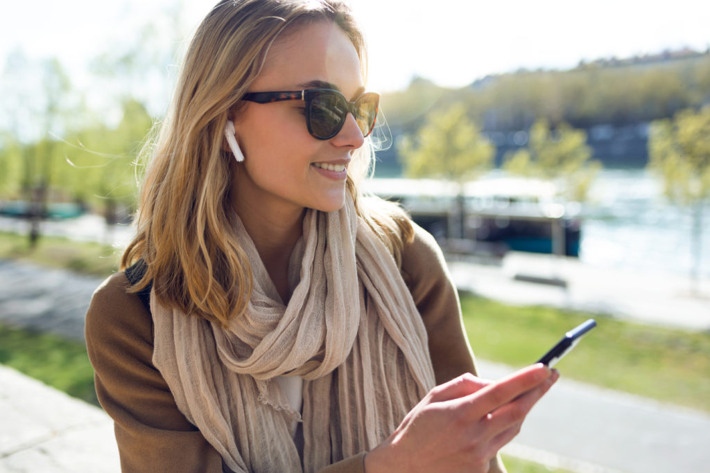 Pretty young woman listening to music with wireless bluetooth earphones and phone.