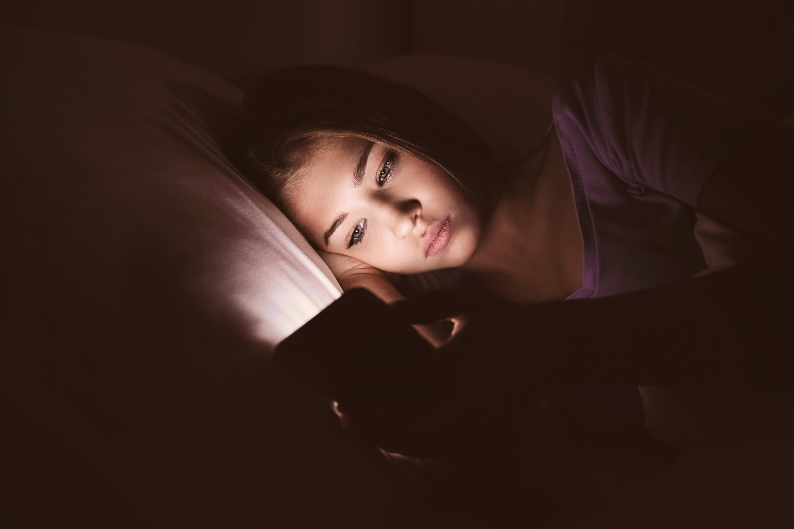 Teenage girl with mobile phone lying in bed at night