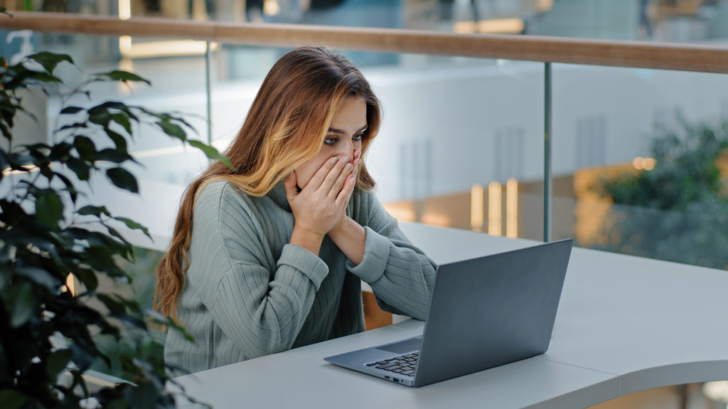 Young woman shocked looking at her laptop.