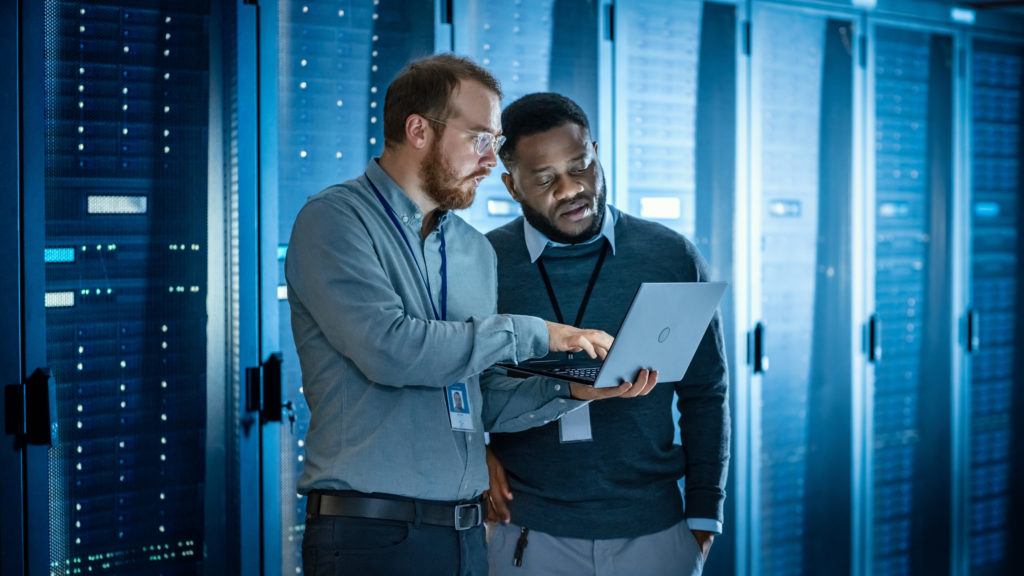 IT colleagues using laptop near server racks.