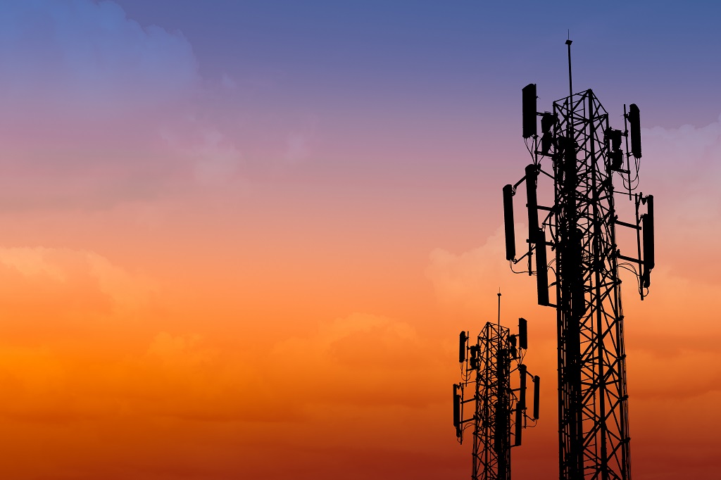 Silhouette of communication towers at dusk against an orange purple sky.