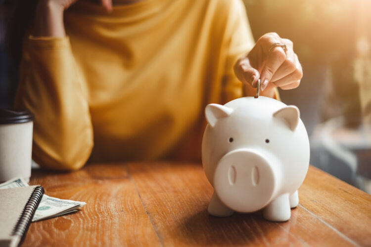 Female hand putting money coin into piggy for saving money.