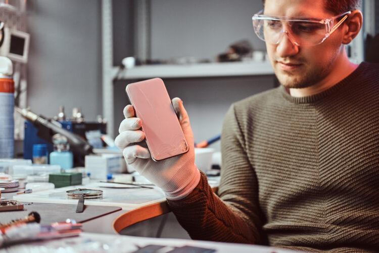 Electronic technician showing a smartphone with a broken body in a repair shop