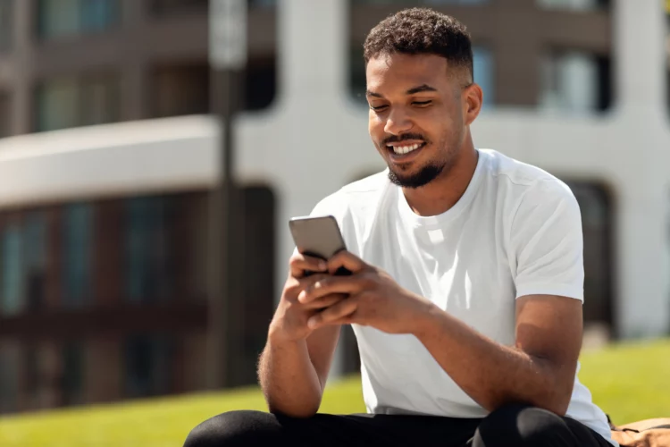 Handsome african american guy using smartphone outdoors while walking in urban city park