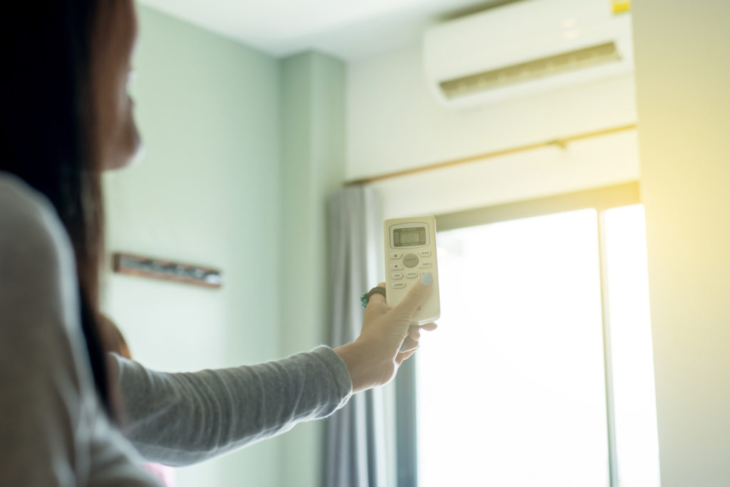 Woman using remote control to open air conditioning in bedroom.