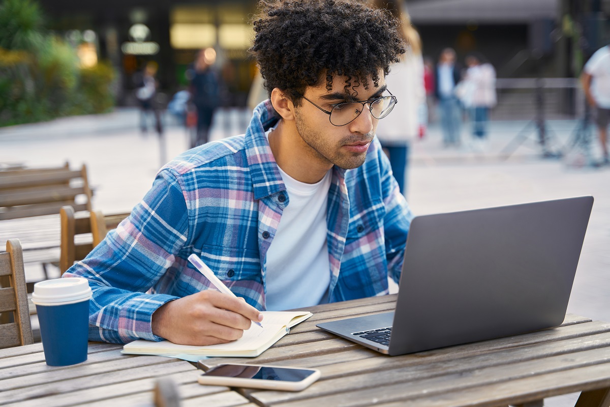 male student with glasses studying outdoor with laptop