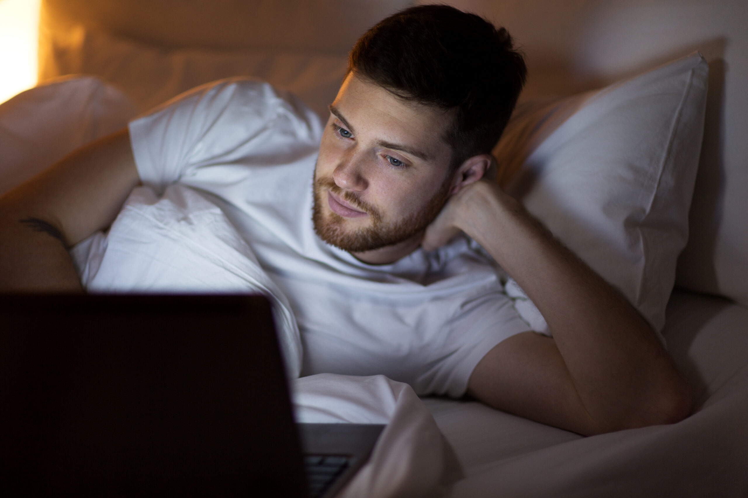 young man with laptop in bed at home bedroom