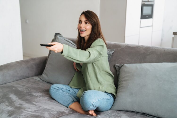 Happy young woman watching tv on sofa