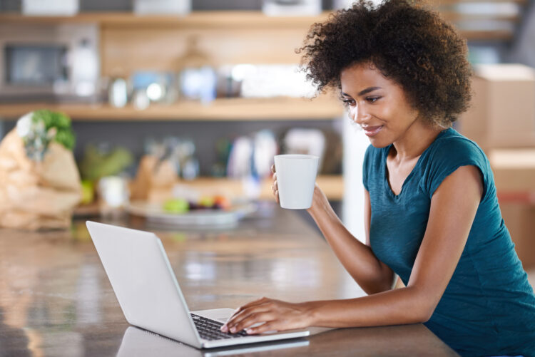 Young woman using a laptop while drinking from a mug.