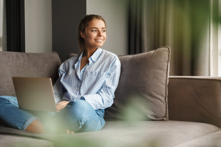 joyful woman using laptop and smiling while sitting on couch