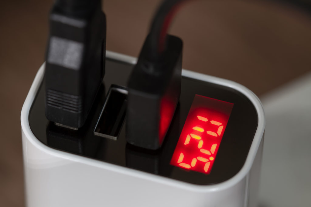 Mobile devices are charging from socket charger for three USB ports output with voltage indicator.