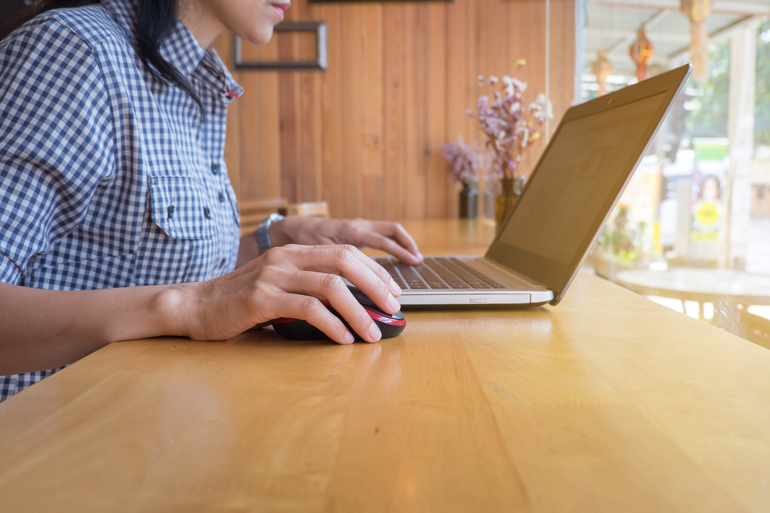 woman's hand clicking on wireless mouse with laptop on wooden table