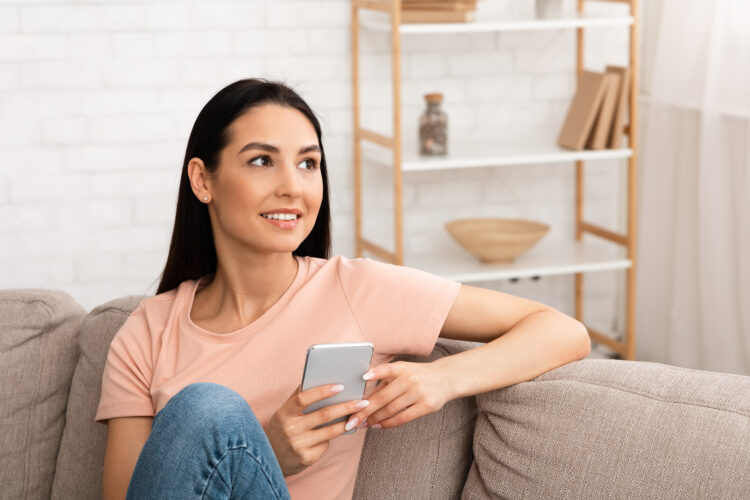 Distracted woman holding mobile phone sitting on the couch